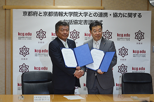 President Wataru Hasegawa (left) and Governor Keiji Yamada of Kyoto Prefecture shake hands after signing a comprehensive agreement on cooperation between KCGI and Kyoto Prefecture on May 26, 2015.
