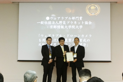 Associate Professor Keiji Emi (center) was awarded the Wearable Category Prize at the 12th Japan e-Learning Awards, Sola City Conference Center, Chiyoda-ku, Tokyo, October 28, 2015.