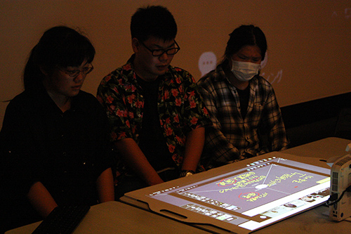 Students of KCG Kyoto Ekimae School looking at the writing of KCG Kamogawa School projected on the desk.