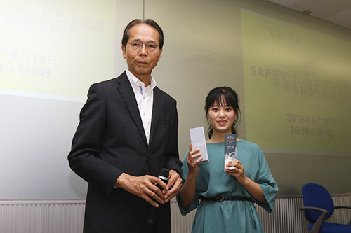 KCGIからのSAP認定試験合格者150人目となった胡さん。藤原正樹教授からSAPジャパンの記念品を受け取りました。