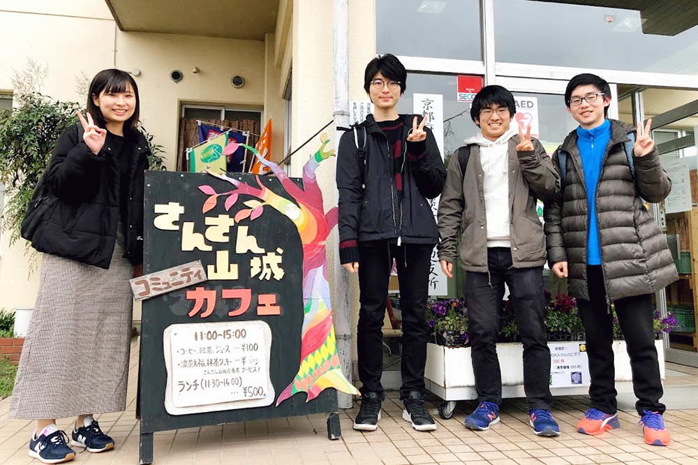 京田辺市のさんさん山城コミュニティカフェ前で，「学生×地域つながる未来プロジェクト」のボランティア学生が記念撮影。一番右が金さん。