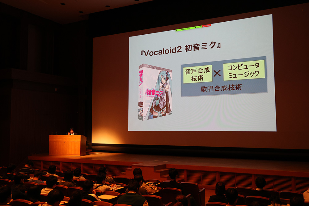 伊藤教授は,バーチャルアイドル「初音ミク」誕生の経緯や成長ぶり,音声技術・ライブ技術への取り組み,国内外での幅広い活躍などについて映像を交え説明しました