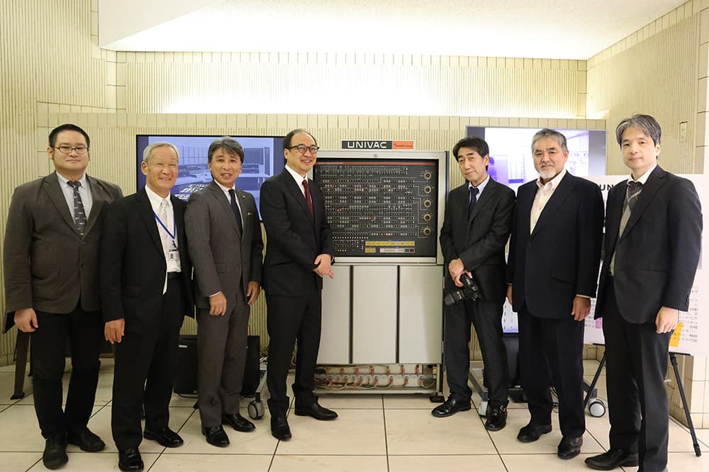 メンテナンスパネルランプが点灯したUNIVAC1100/20の展示の前でプロジェクトメンバーが記念撮影(同,KCG京都駅前校 KCGコンピュータミュージアム)