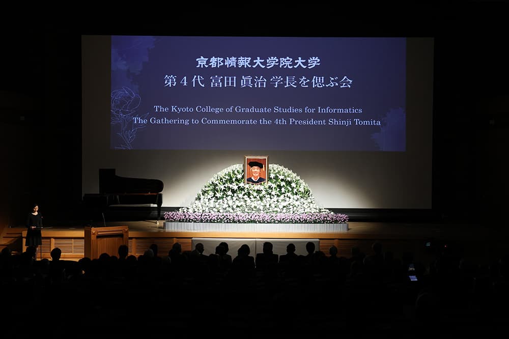 第４代富田眞治学長を偲ぶ会。富田先生が優しくほほ笑む写真が飾られました（2025年1月25日，京都情報大学院大学京都駅前サテライト・京都コンピュータ学院京都駅前校大ホール）
